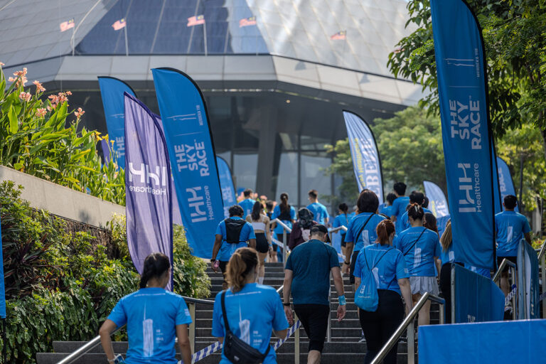 Climbers in blue Sky Race tees walk up the steps to Merdeka 118 past IHH Healthcare and Sky Race flags
