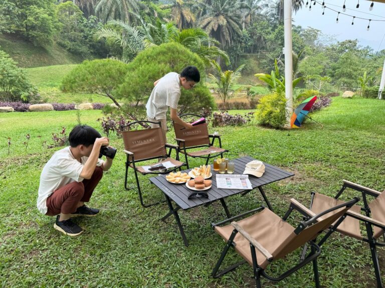 A Creo intern crouches to photograph an afternoon tea table with Sementra chairs on the lawn while another adjusts the props